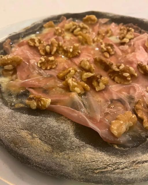 Pizza con impasto nero al carbone vegetale, prosciutto crudo e gherigli di noce