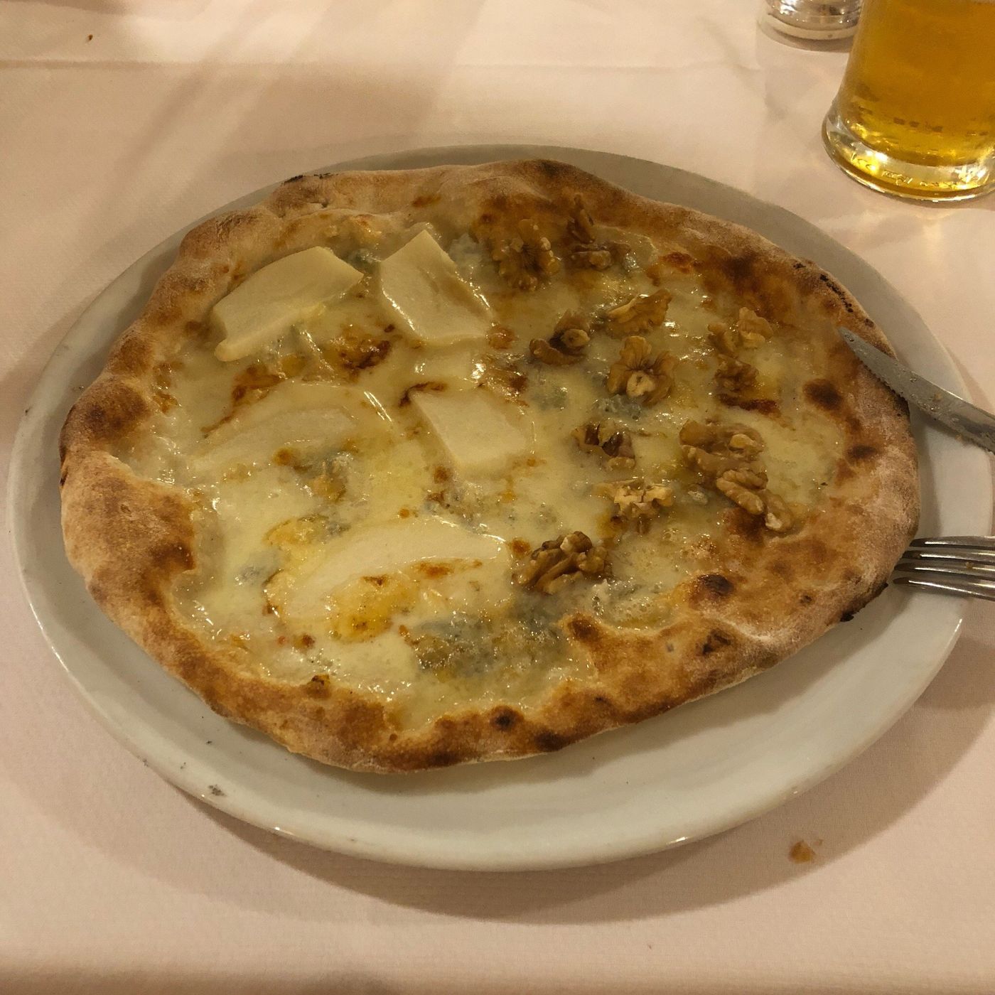 Pizza bianca con formaggio erborinato, fette di pera e noci, accanto a un boccale di birra