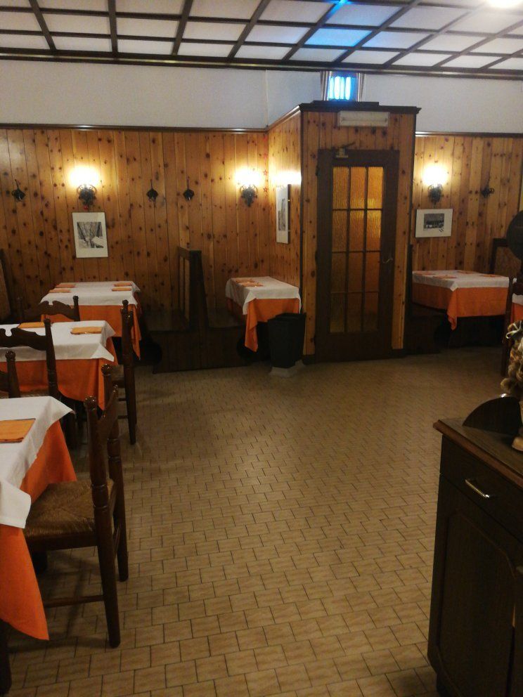 Sala con pareti rivestite in perlinato di legno, applique e tavoli apparecchiati con tovaglie arancioni